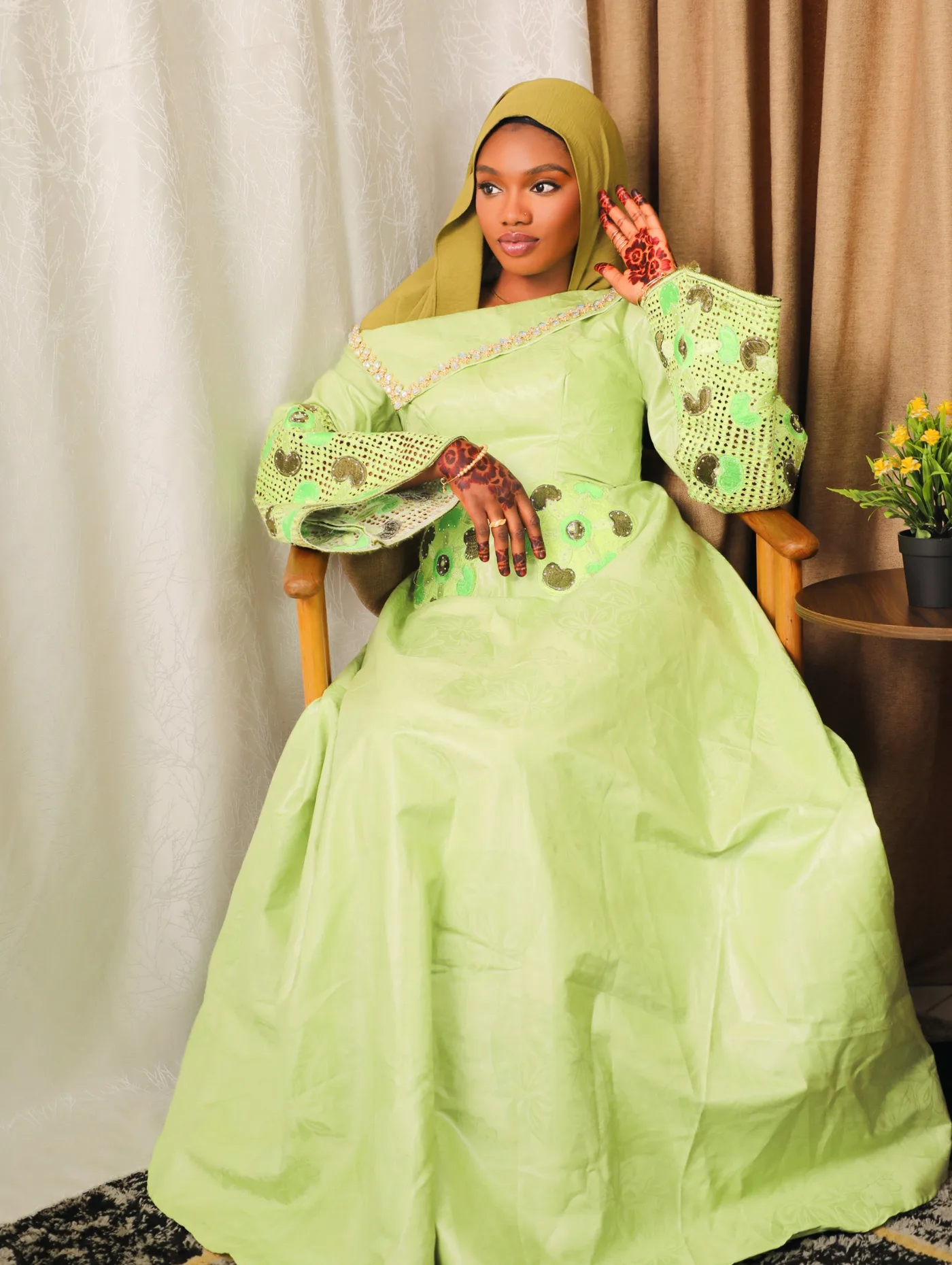 Portrait en studio d'une femme en robe verte brodée et voile, assise sur un fauteuil en bois